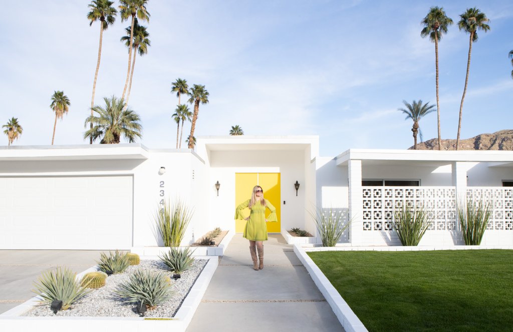 a women standing in front of a house with a yellow door