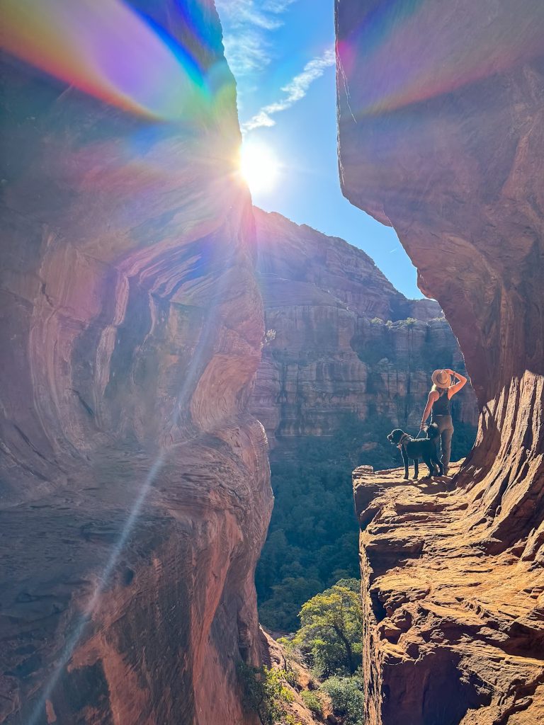 a women and a dog standing at the ledge of Subway Cave in Sedona, AZ