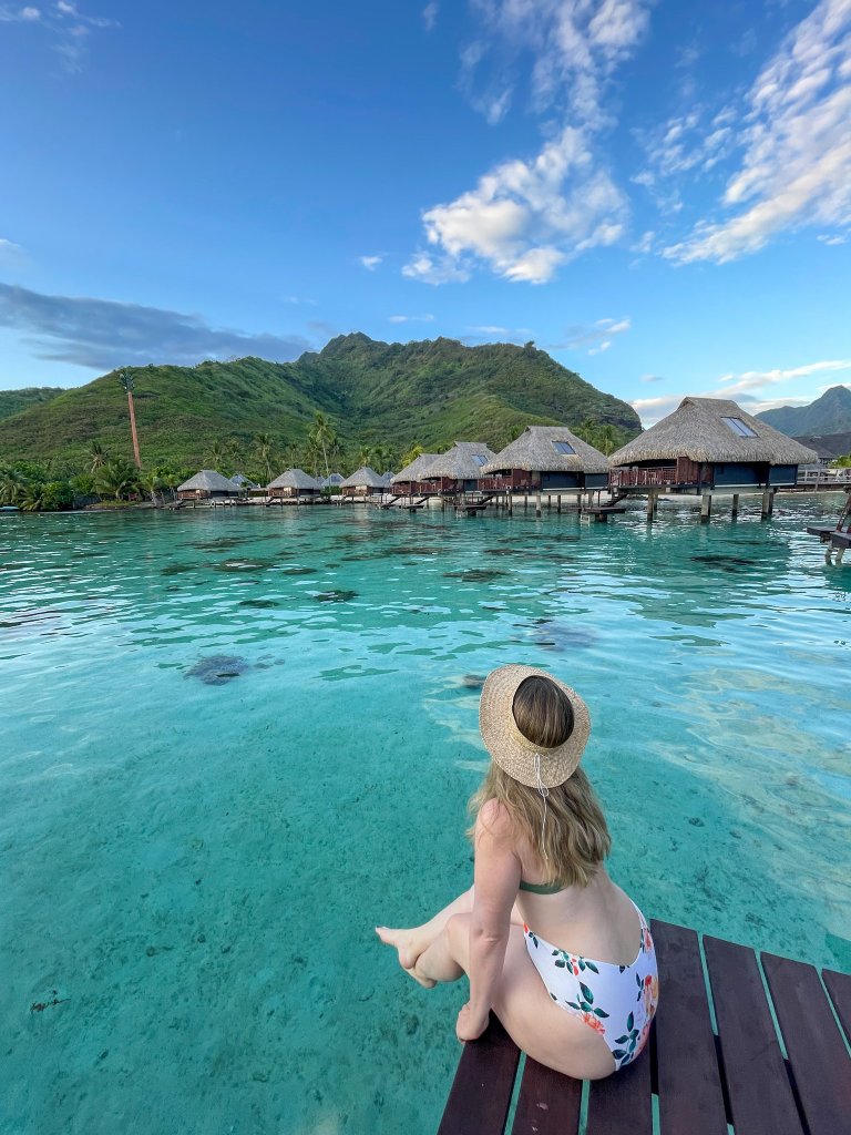 a women sitting on a dock looking at over water bungalows