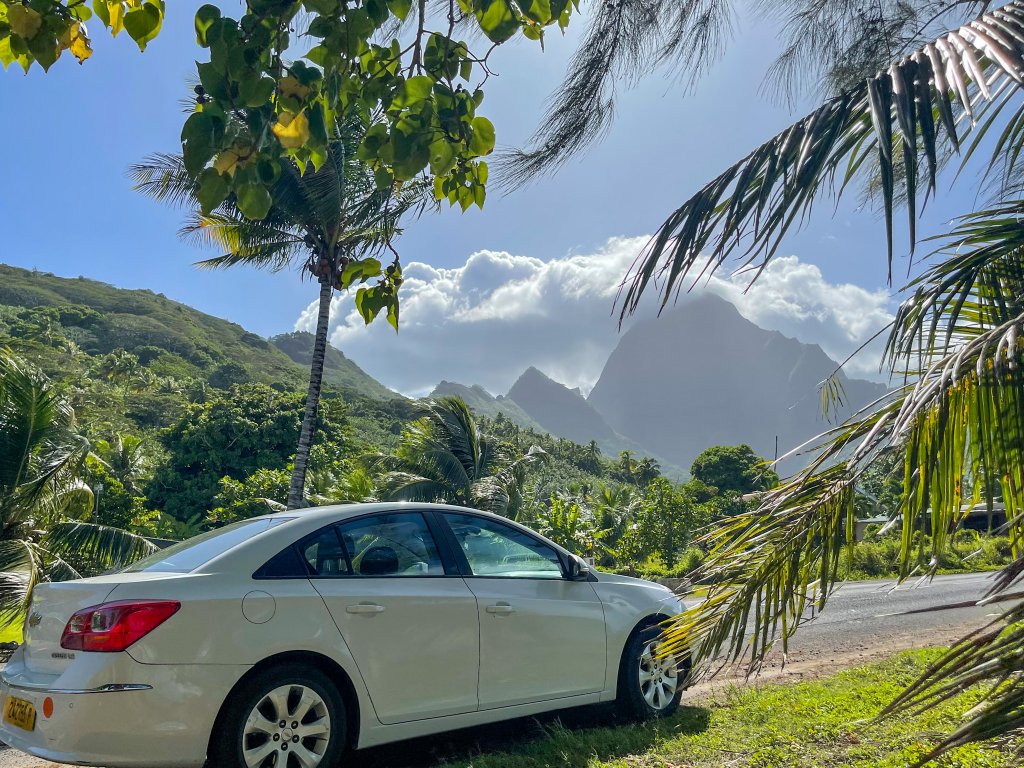 a white car on the side. ofthe road with a mountain in the back ground  