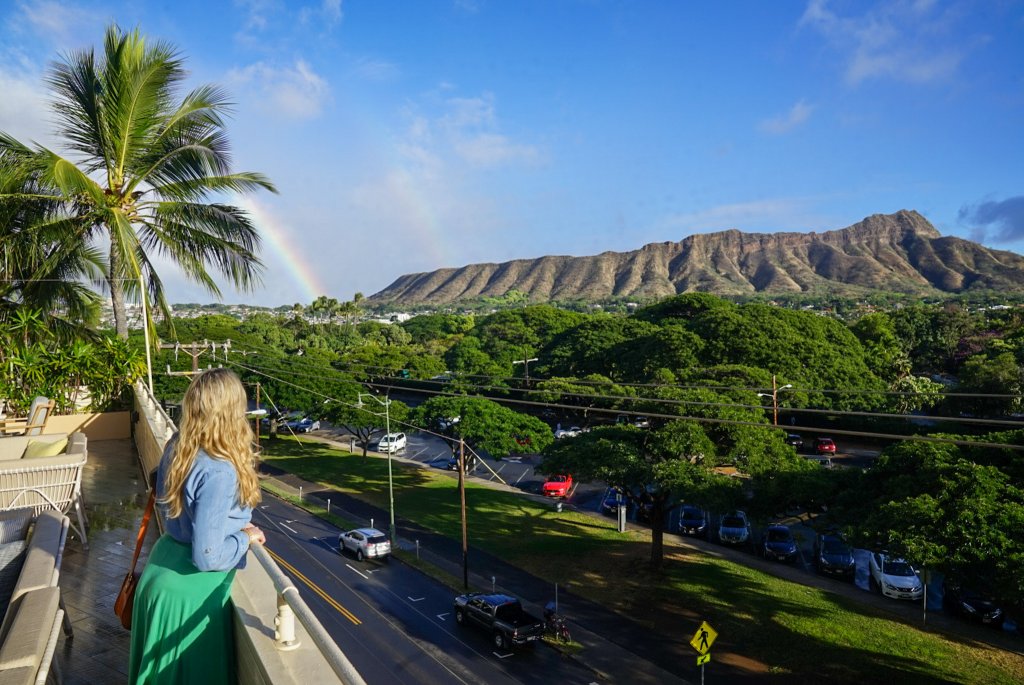 a woman looking at Diamond Head mountain with a rainbow next to it 